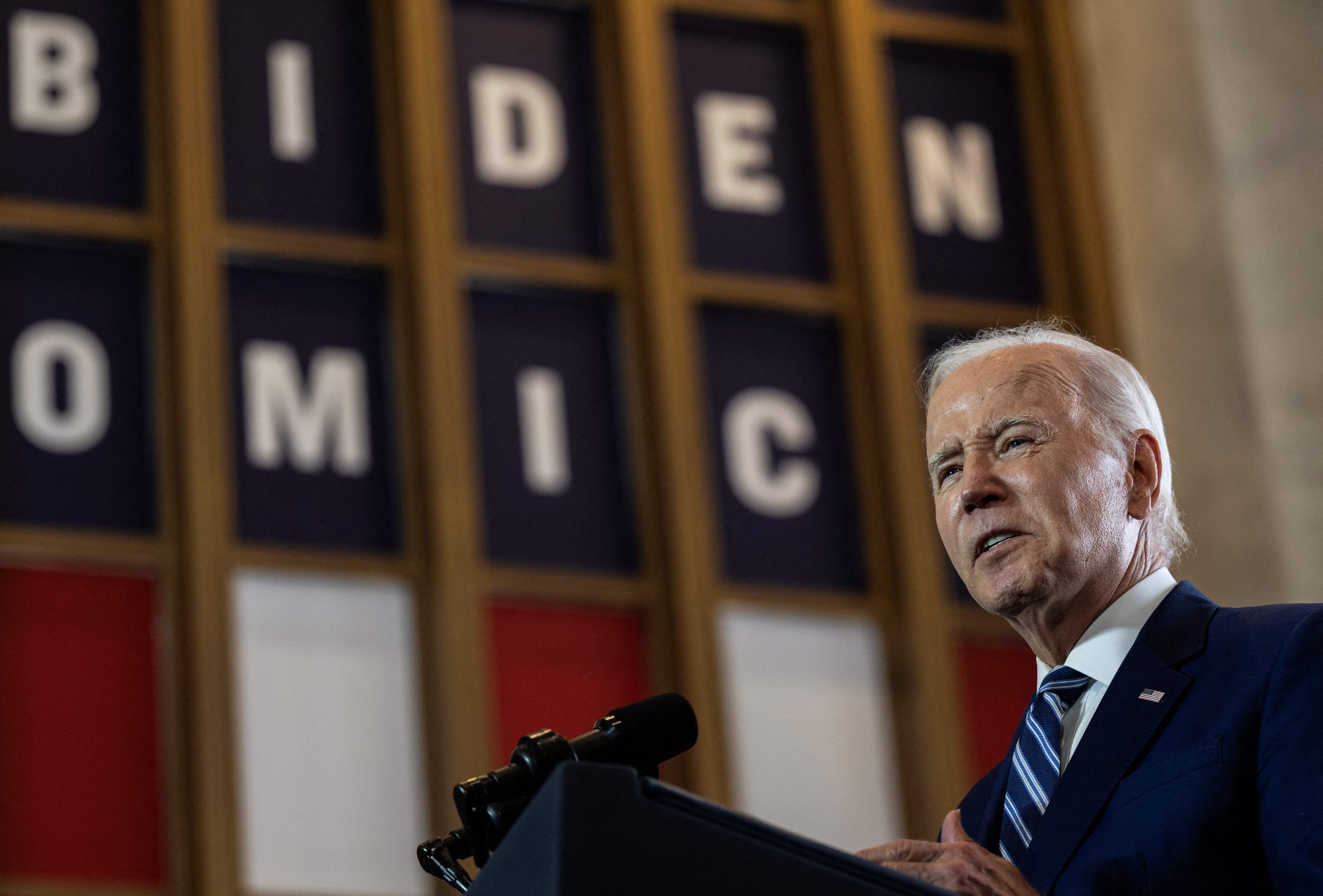 President Joe Biden speaks with a banner reading 