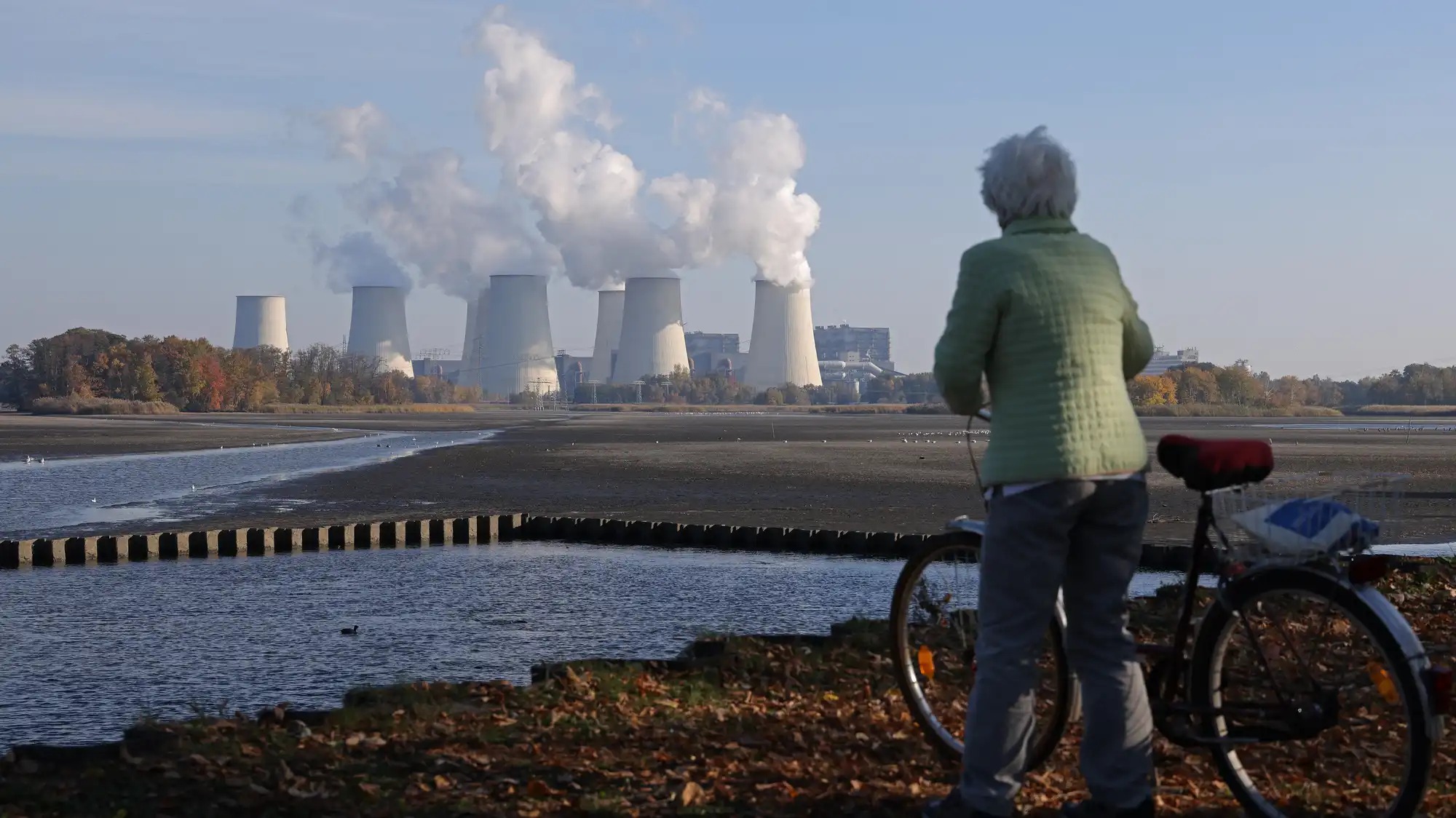 An older woman with a bike looks out at a nuclear plant in the distance.