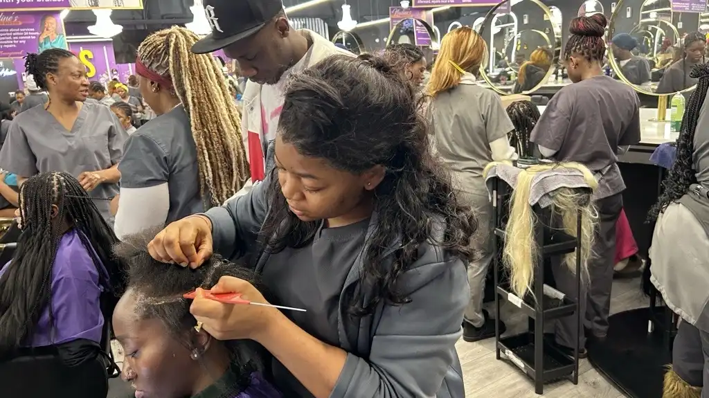 A woman braids hair in a crowded salon.