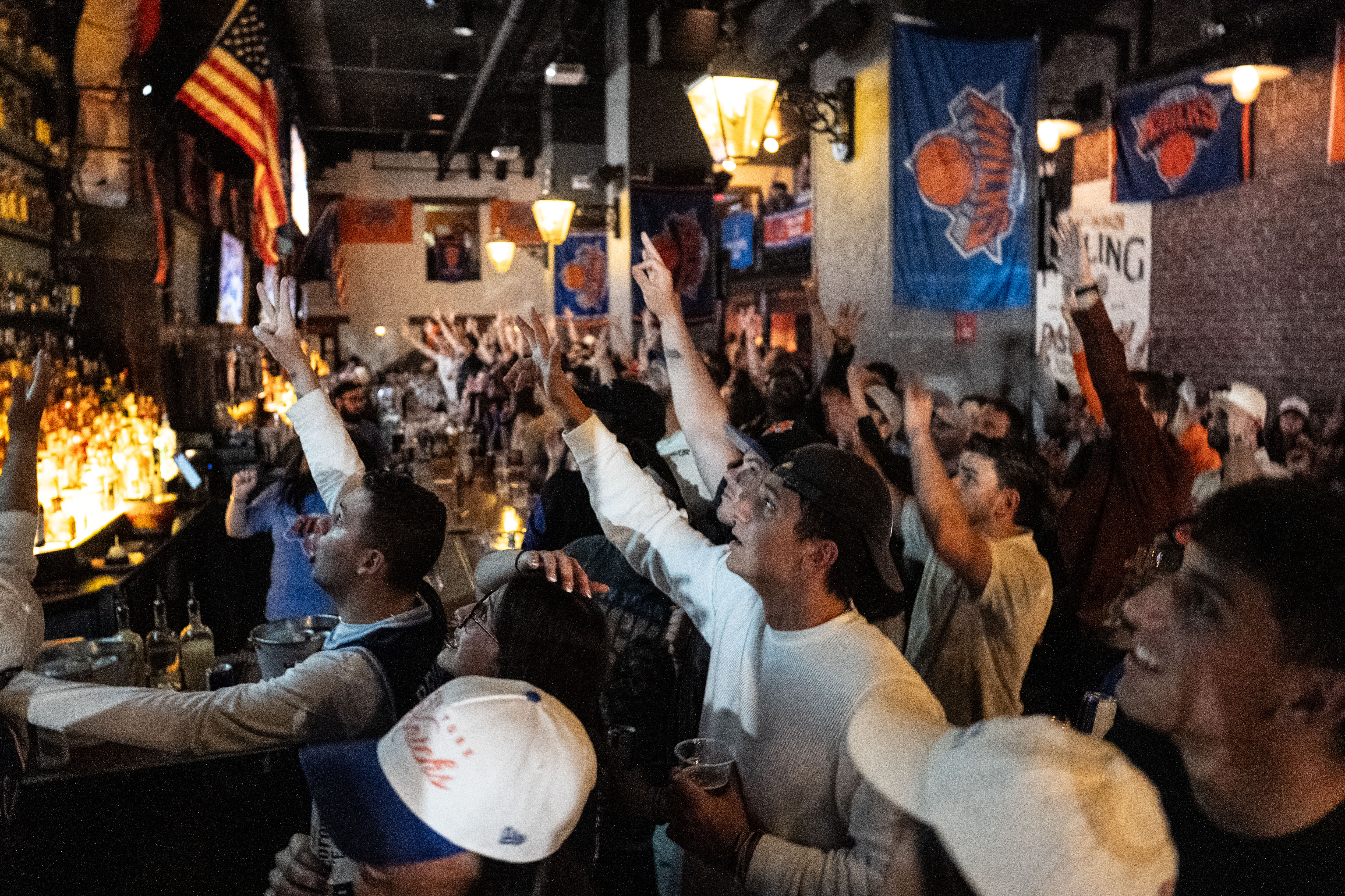 Fans cheer with arms raised while watching a Knicks game at a New York bar. 