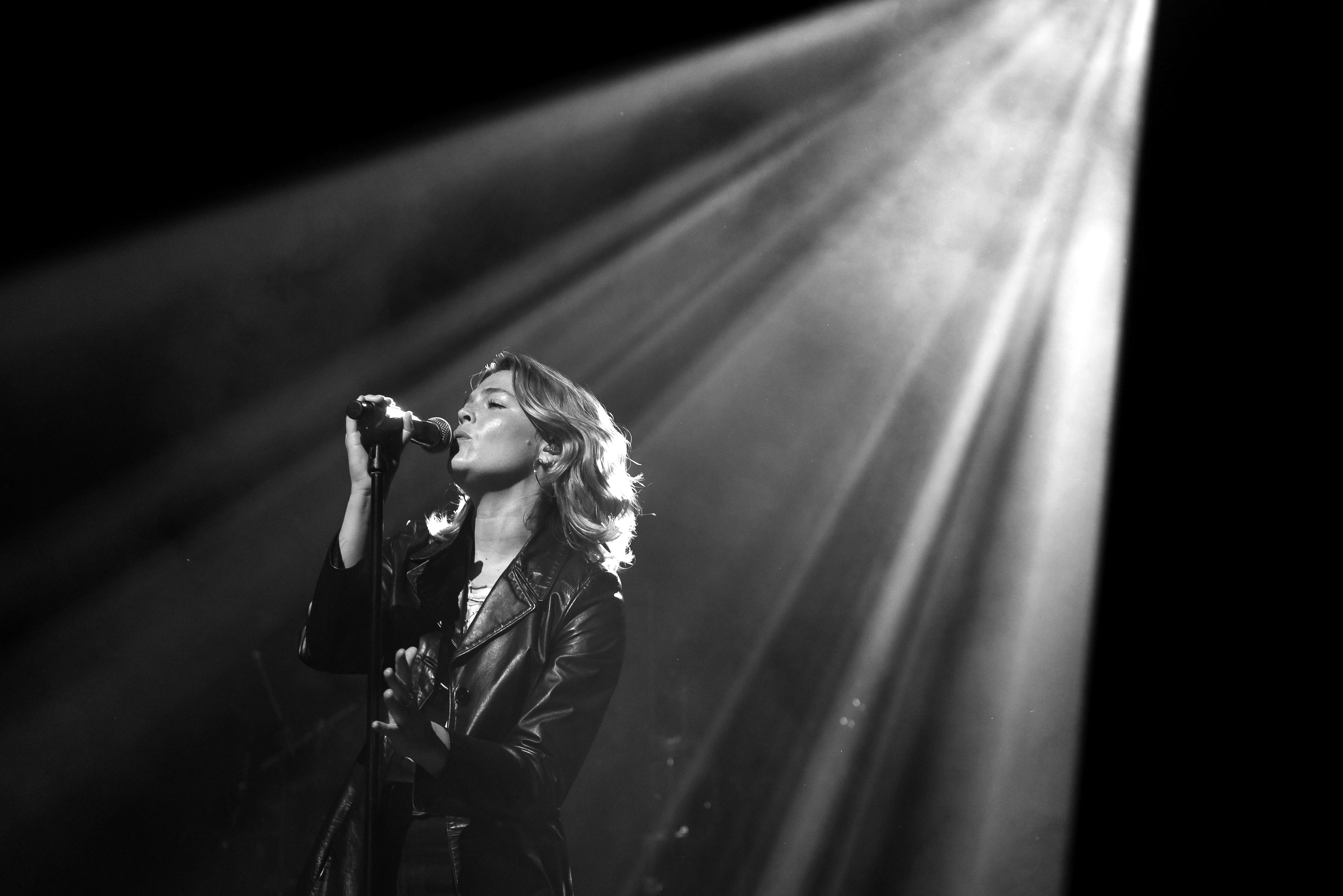 Maggie Rogers sings under a spotlight in a black and white photo.
