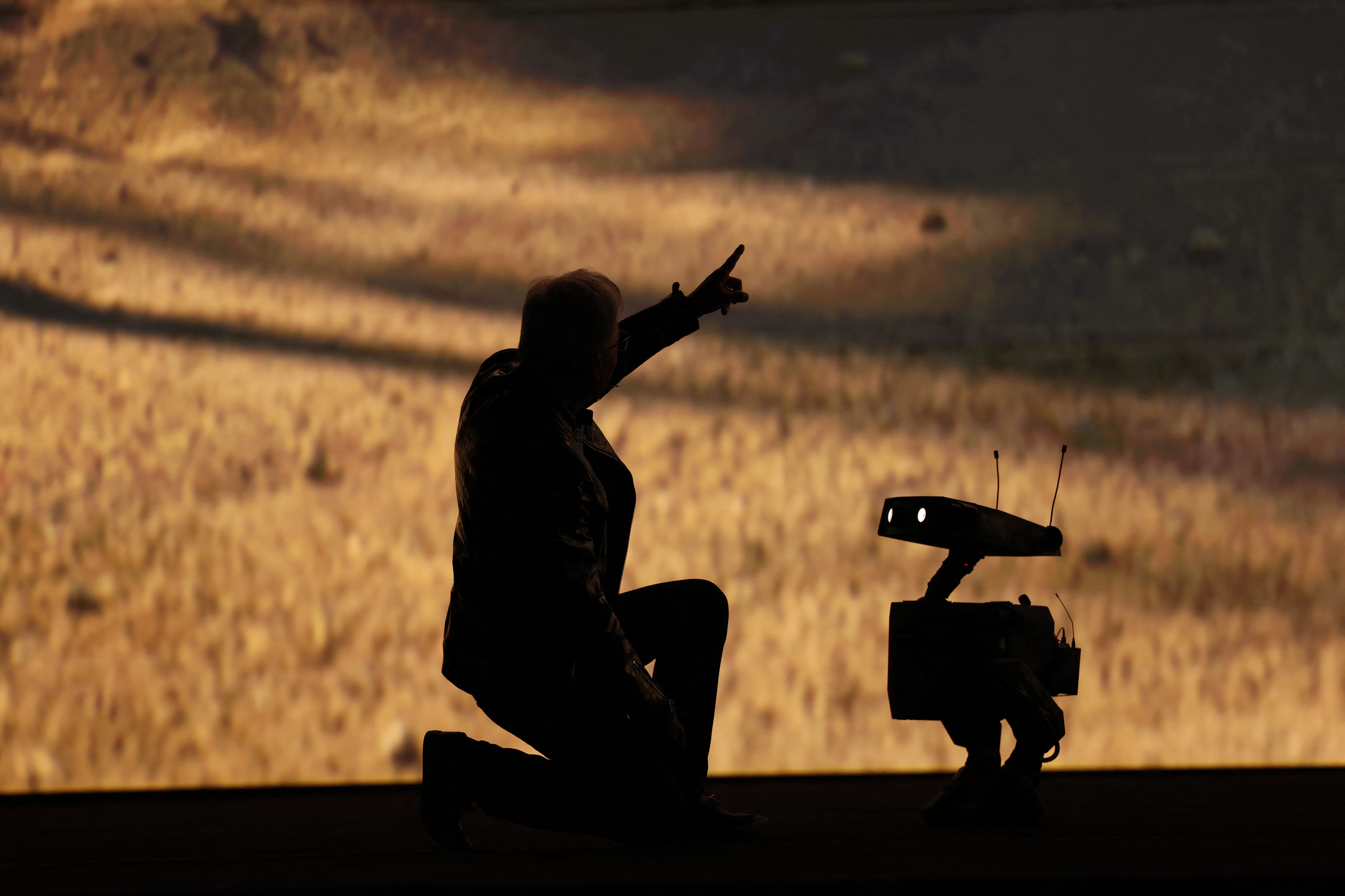 Jensen Huang speaks with a robot in silhouette onstage at CES.