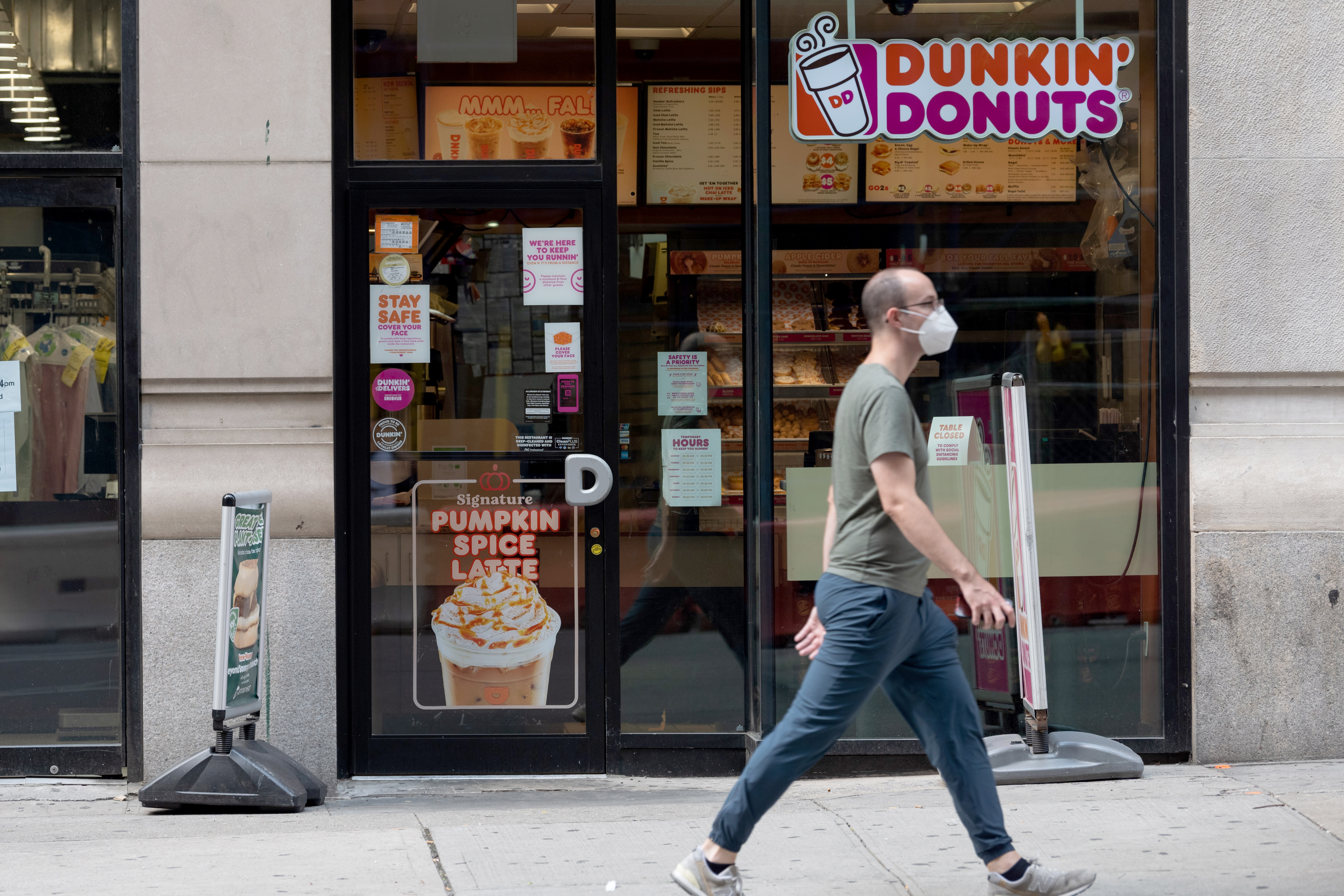 A man passes a Dunkin advertising a pumpkin spice latte