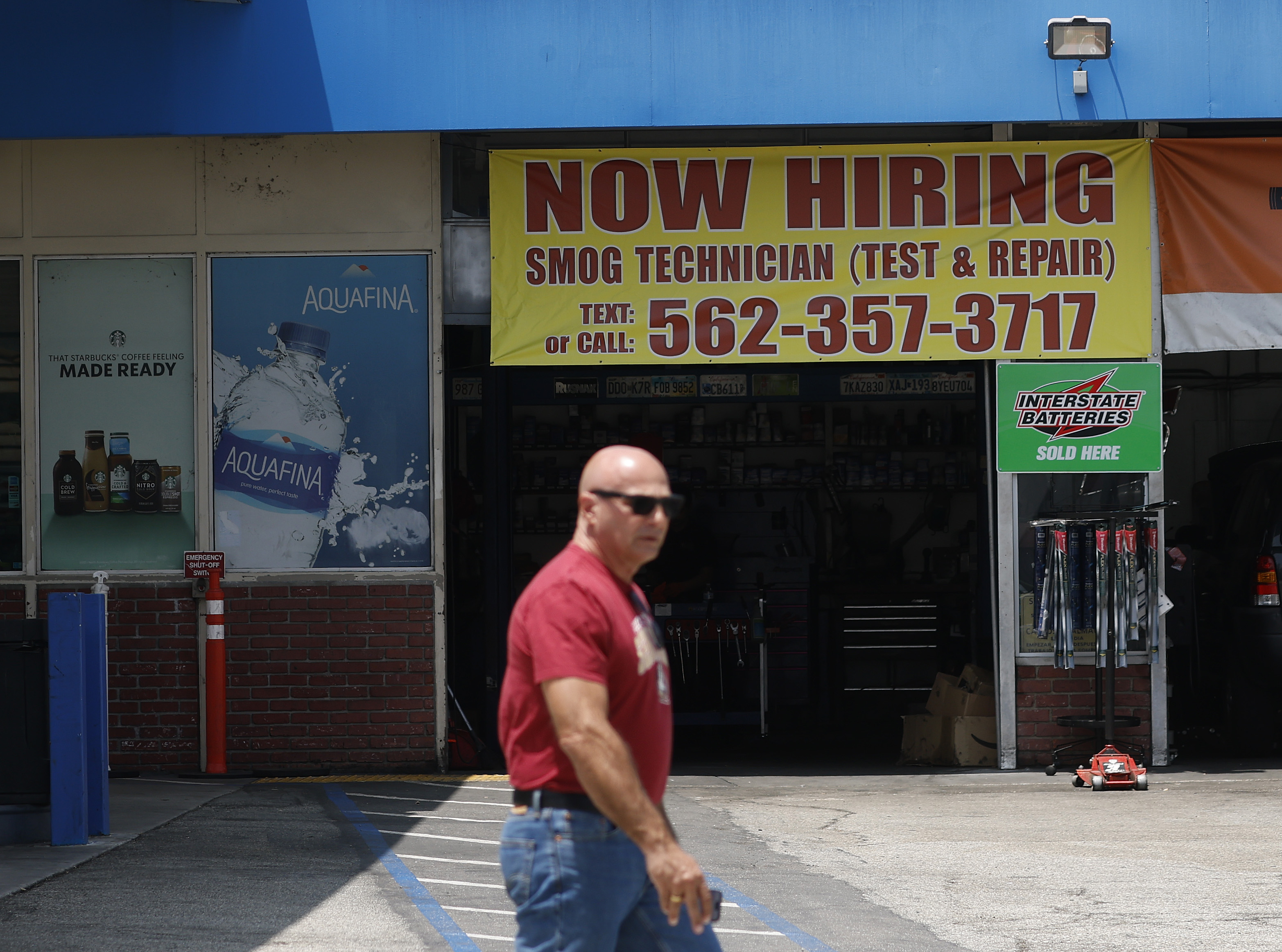 A man walks by a shop advertising a smog technician job.
