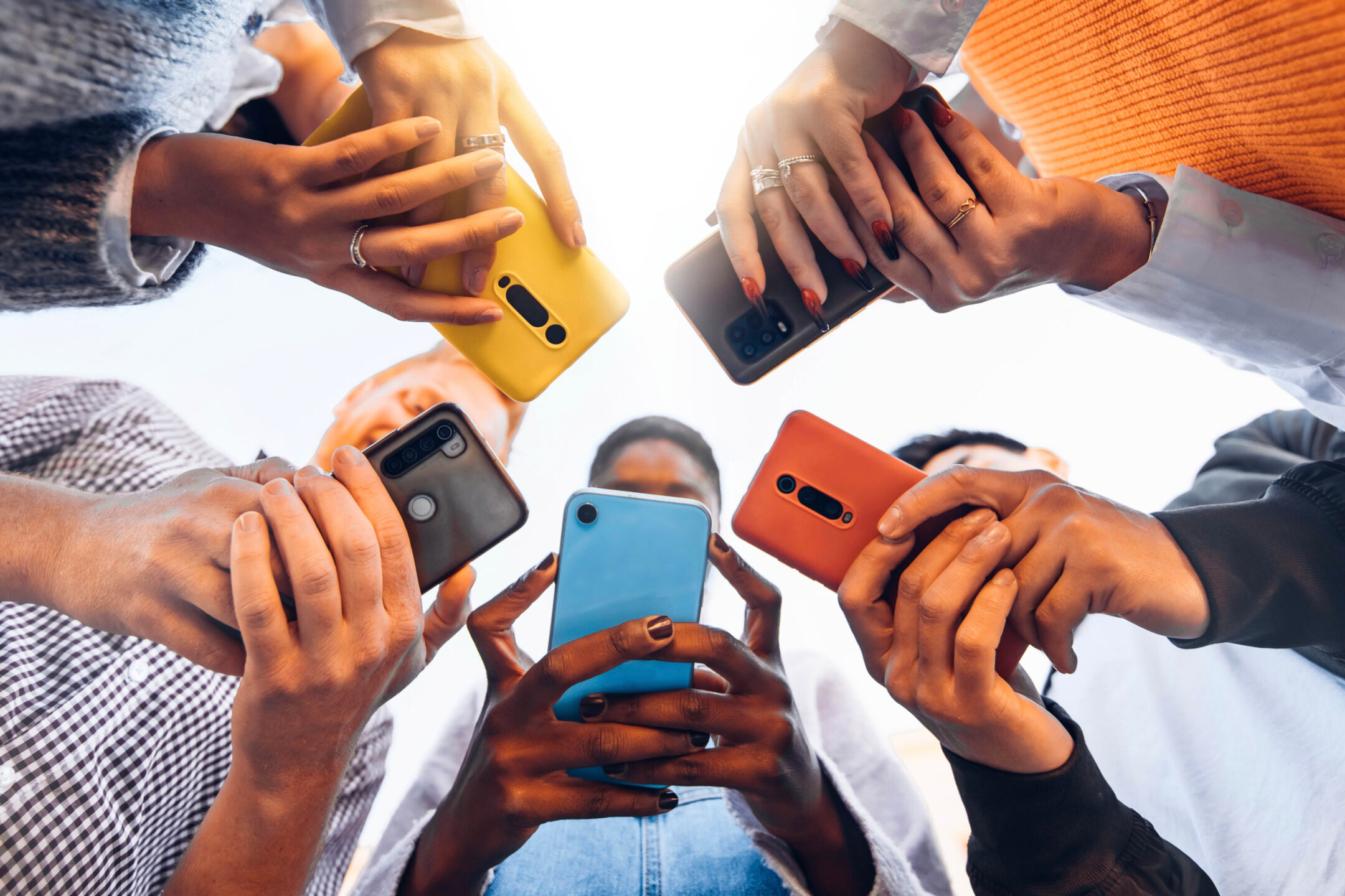 Five people huddle close together. They are all holding their cellphones with two hands and looking at the screen. 