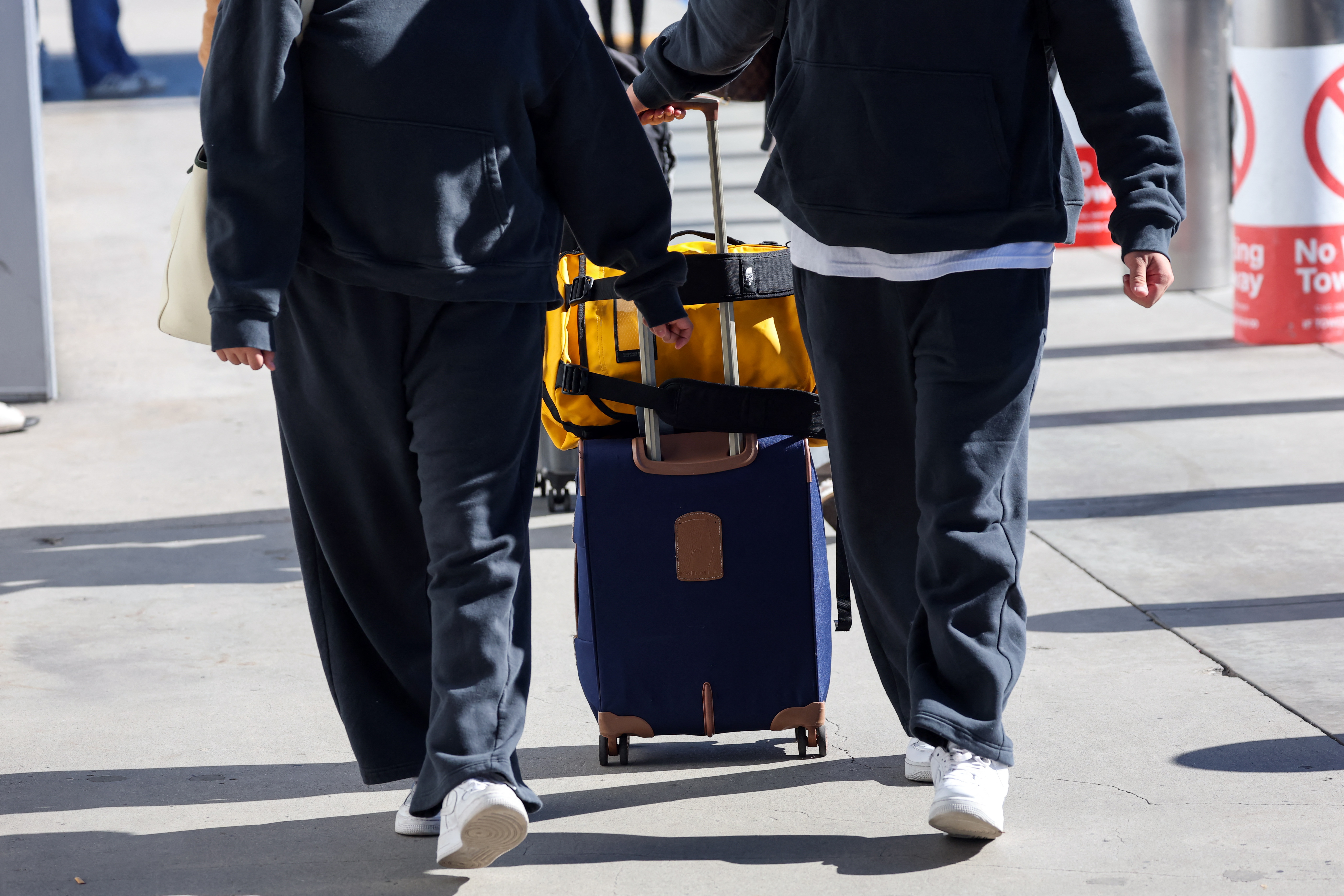 Two travelers in matching sweatpants wheel bags through an airport.