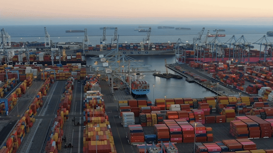 A port with stacks of shipping containers and several cranes near the waterfront.