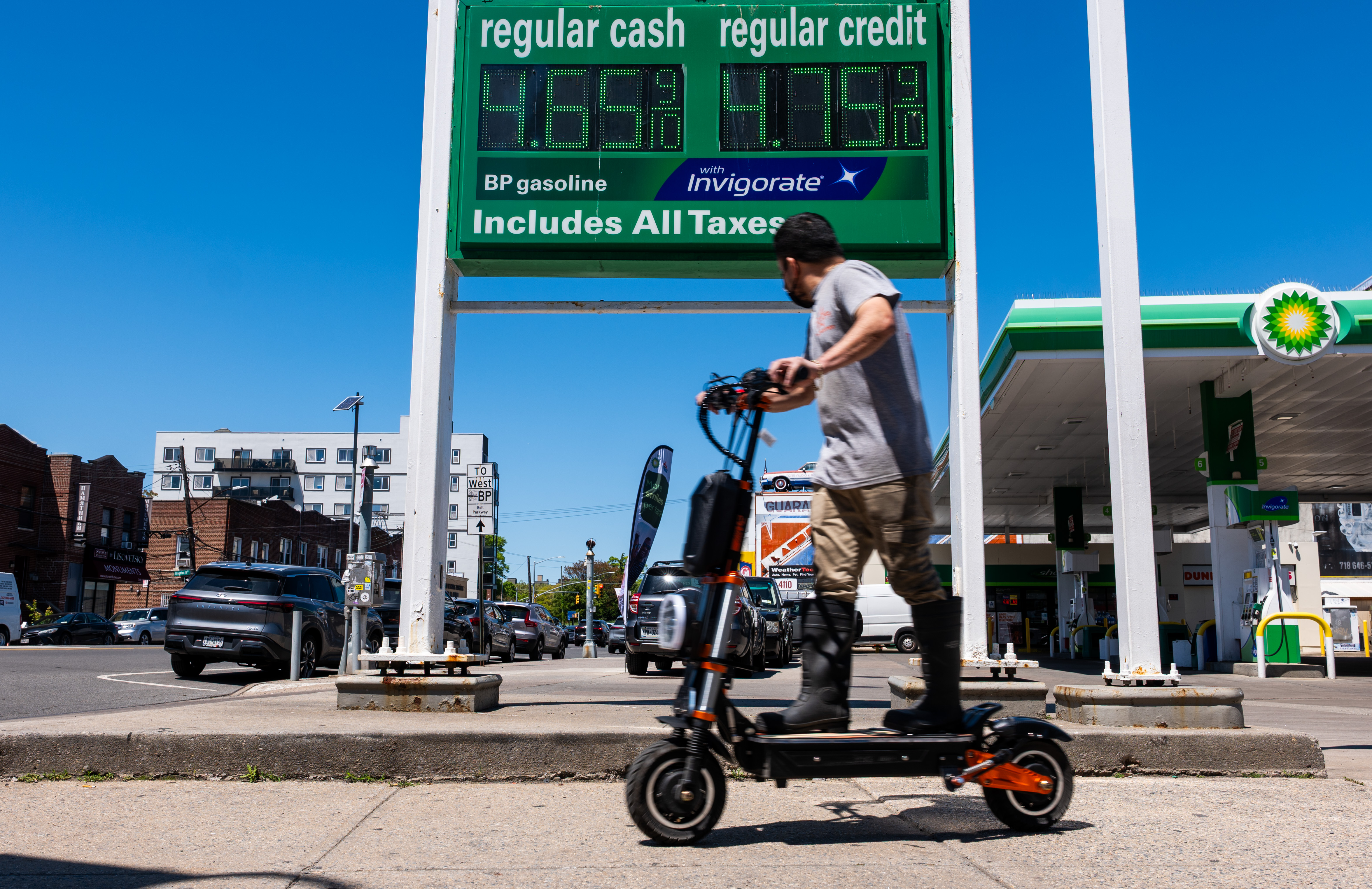 A man rides a scooter past a gas station advertising $4.65 a gallon for regular.