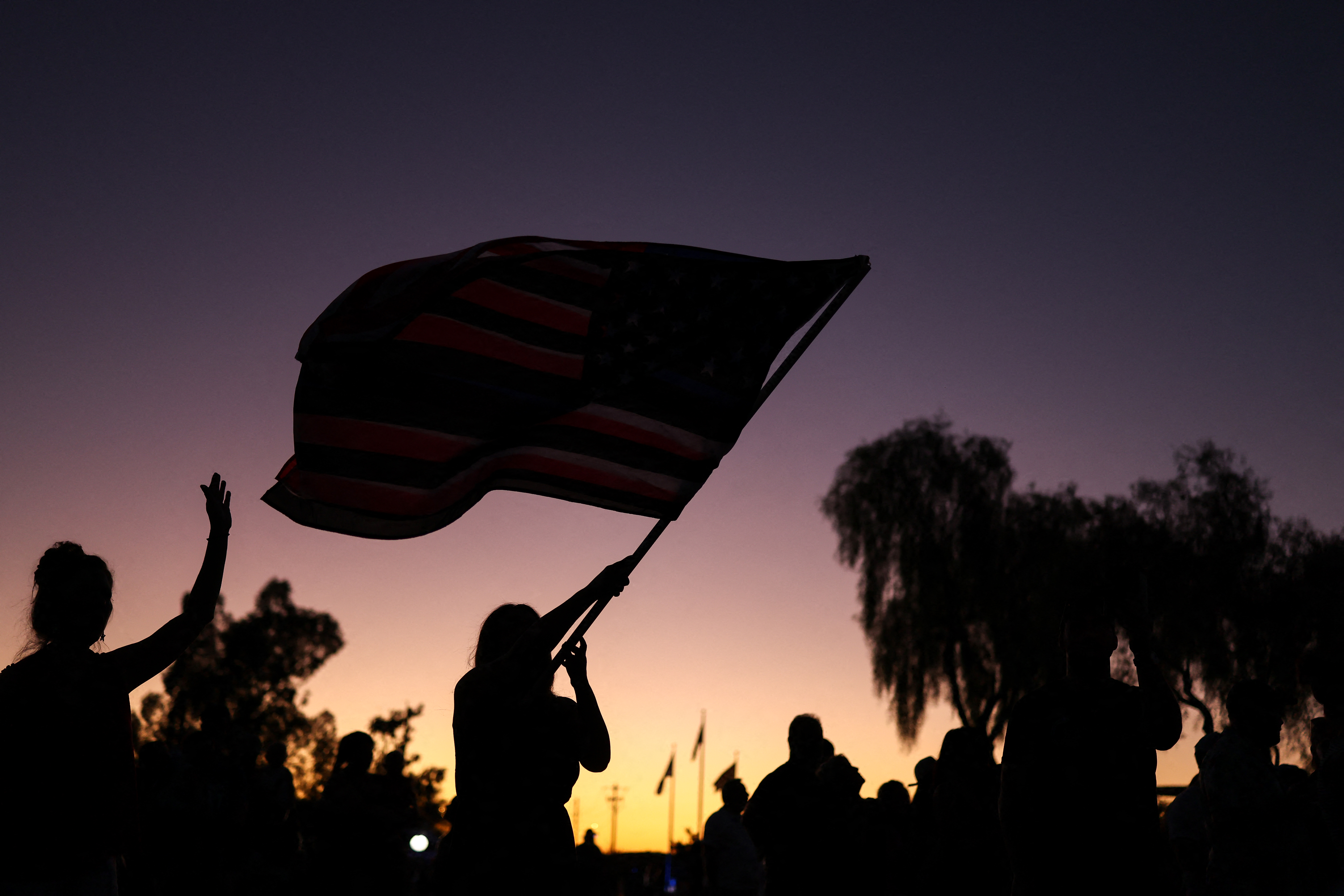 A woman waves a flag at dusk during a memorial for Charlie Kirk.
