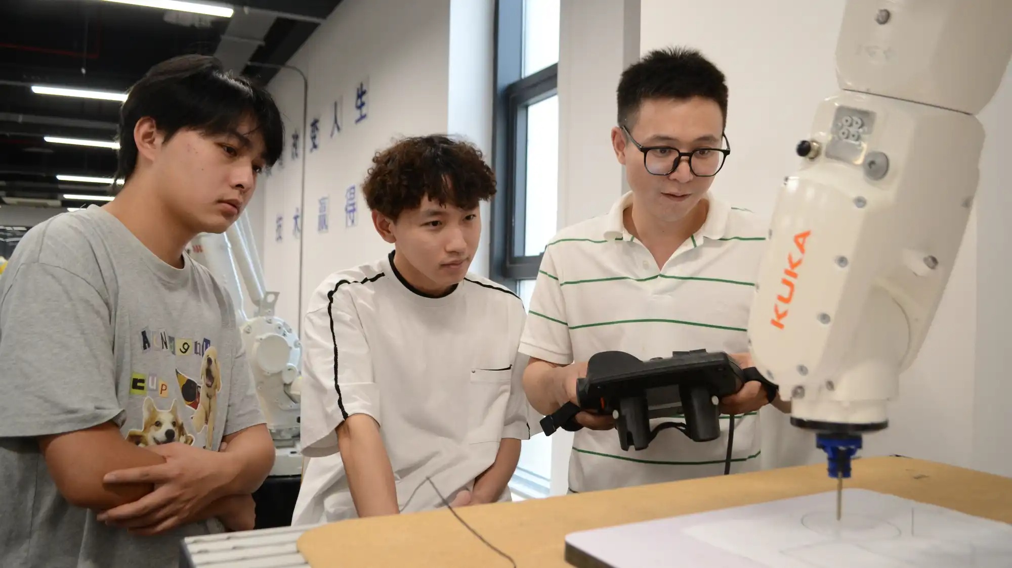 Three young men operate a robotic arm.