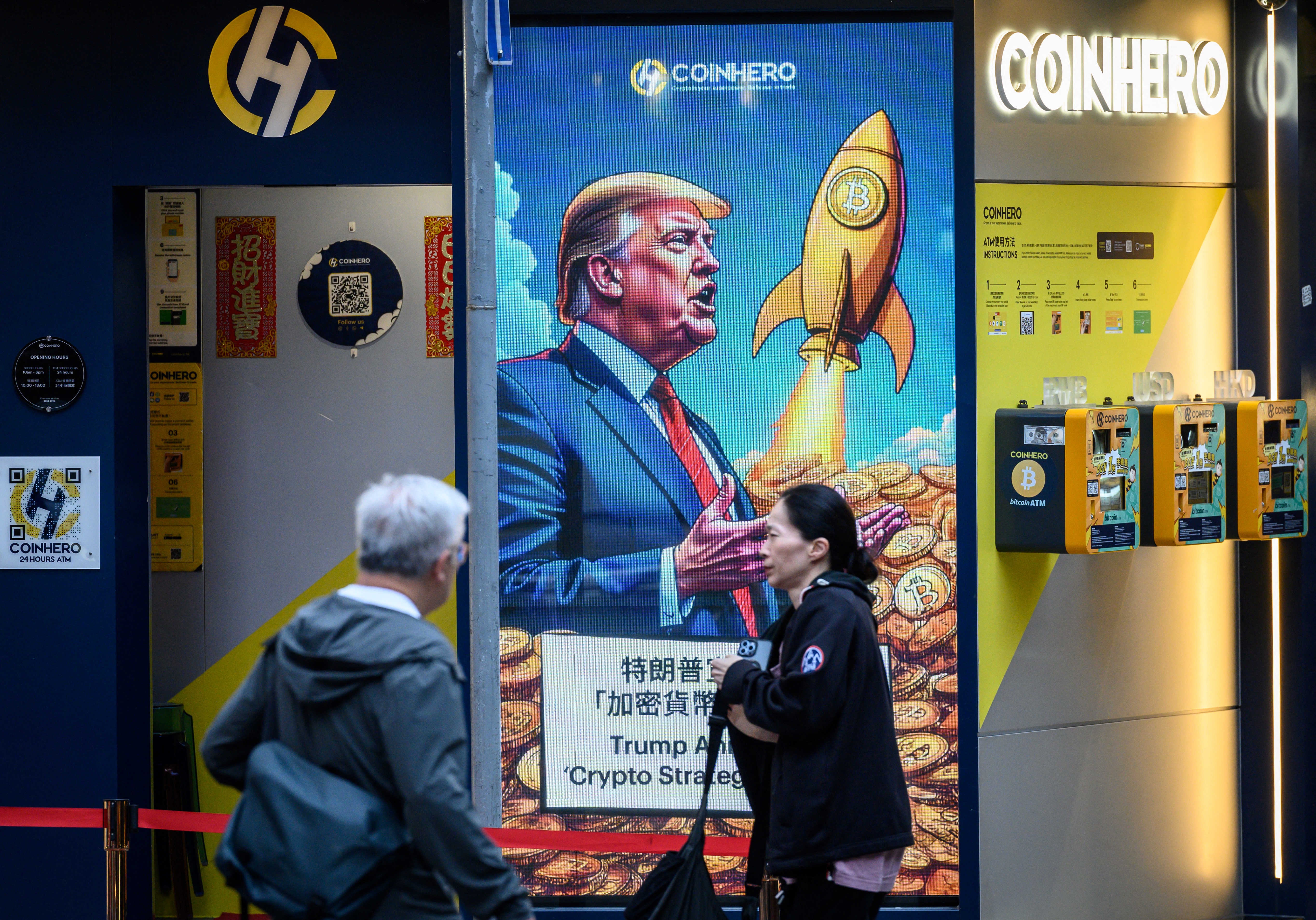 People walk past a cryptocurrency exchange office with a screen featuring US President Donald Trump holding cryptocurrency coins in Hong Kong on March 12, 2025.