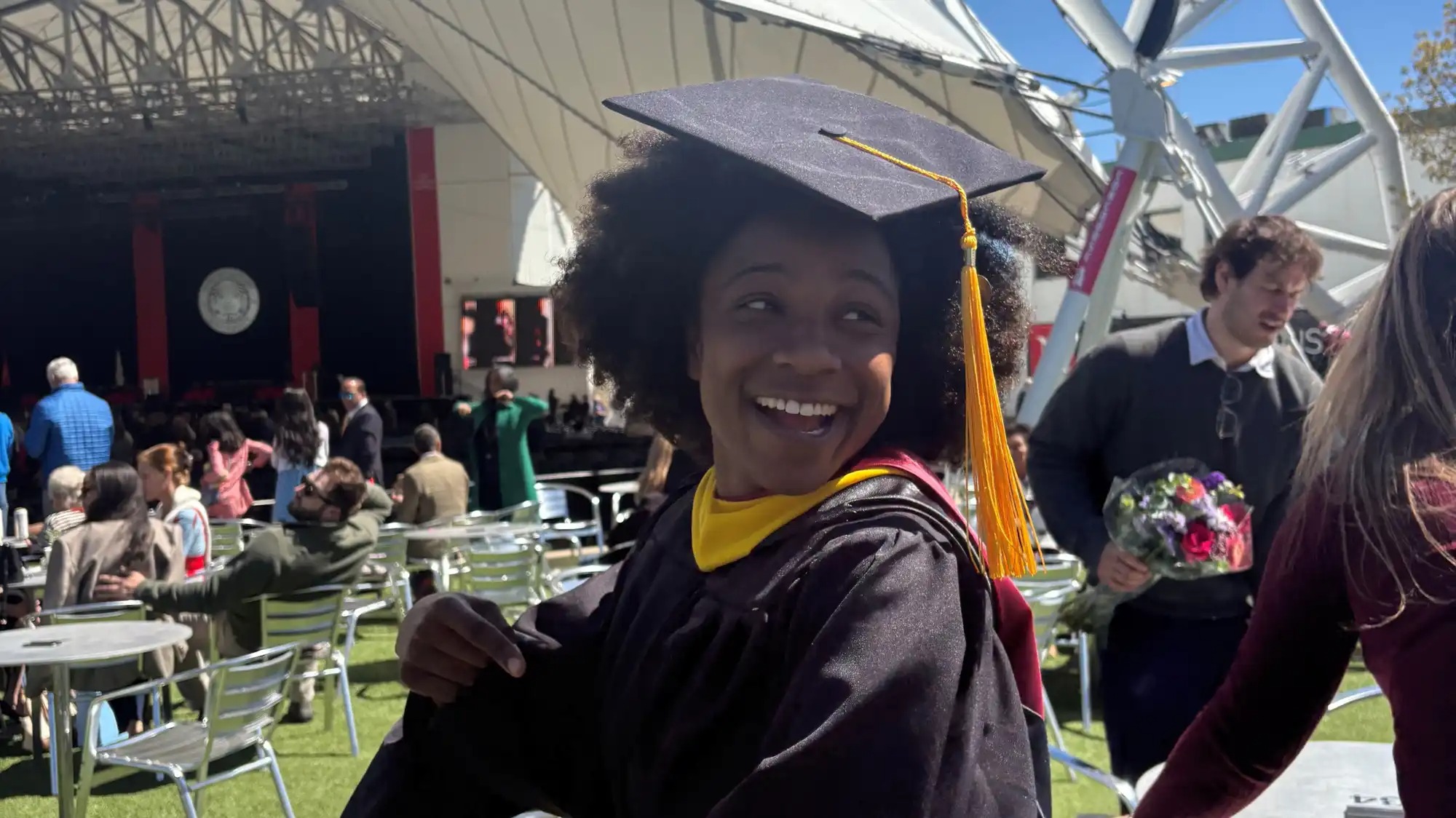 A young woman in a cap and gown smiles in a candid photo at a graduation ceromony.