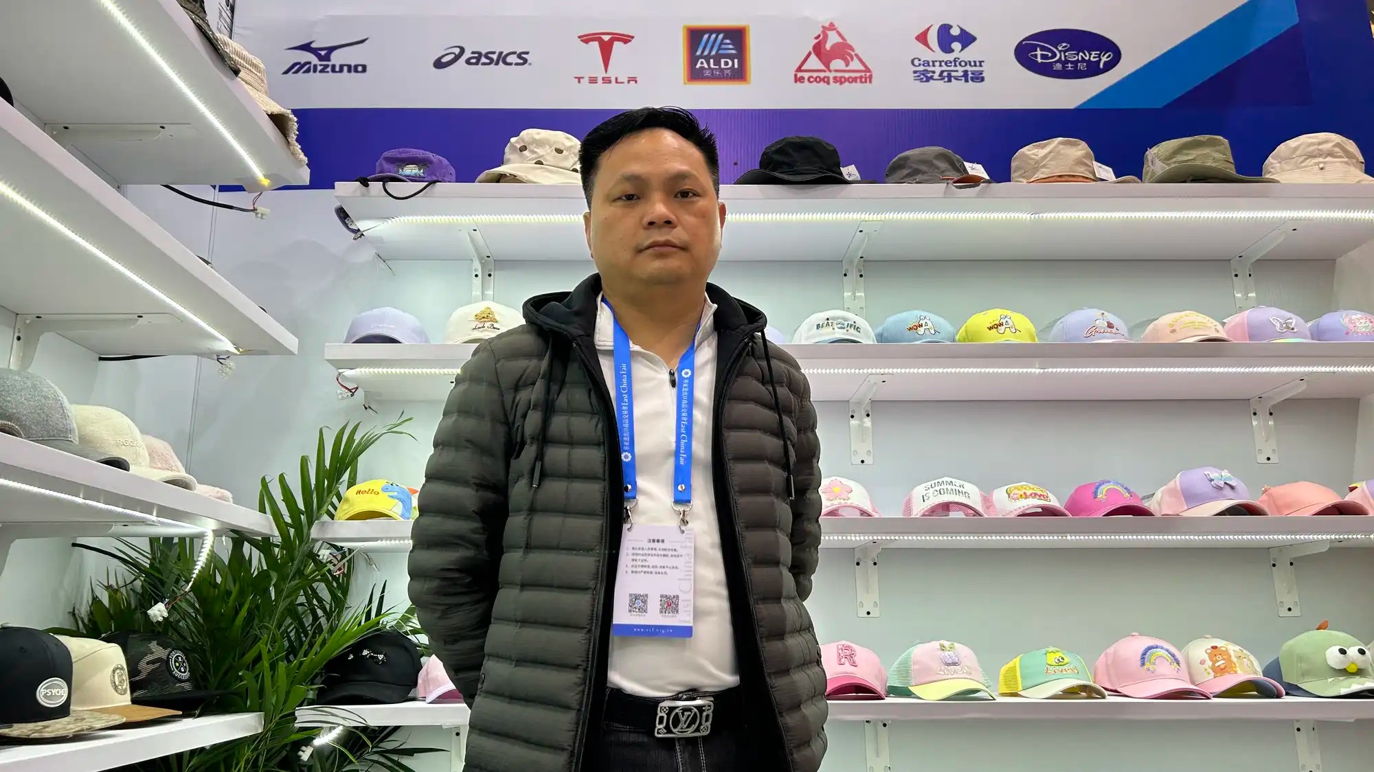 A man stands in front of a display of hats at a trade show.