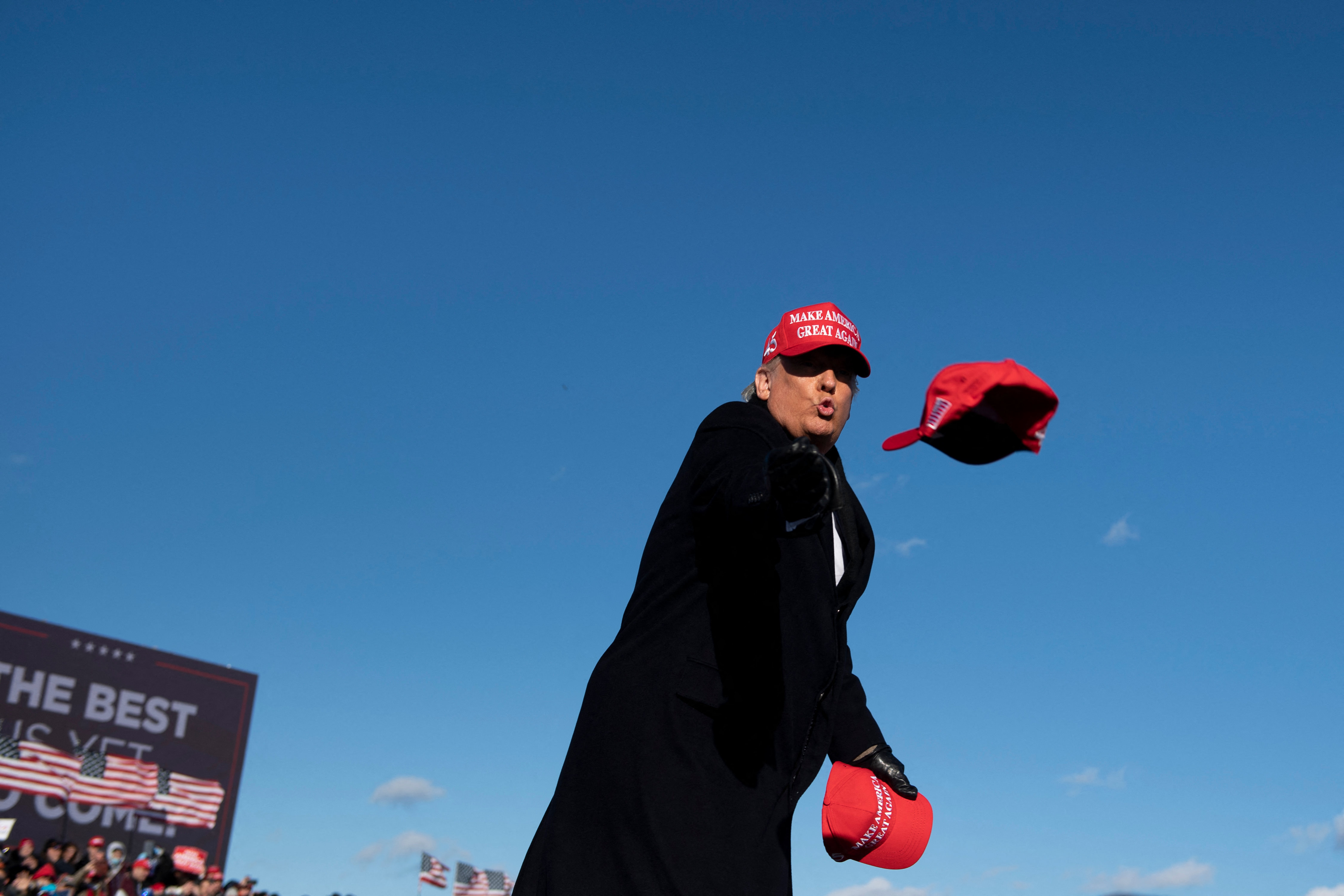 President Donald Trump throws a red hat to a crowd.