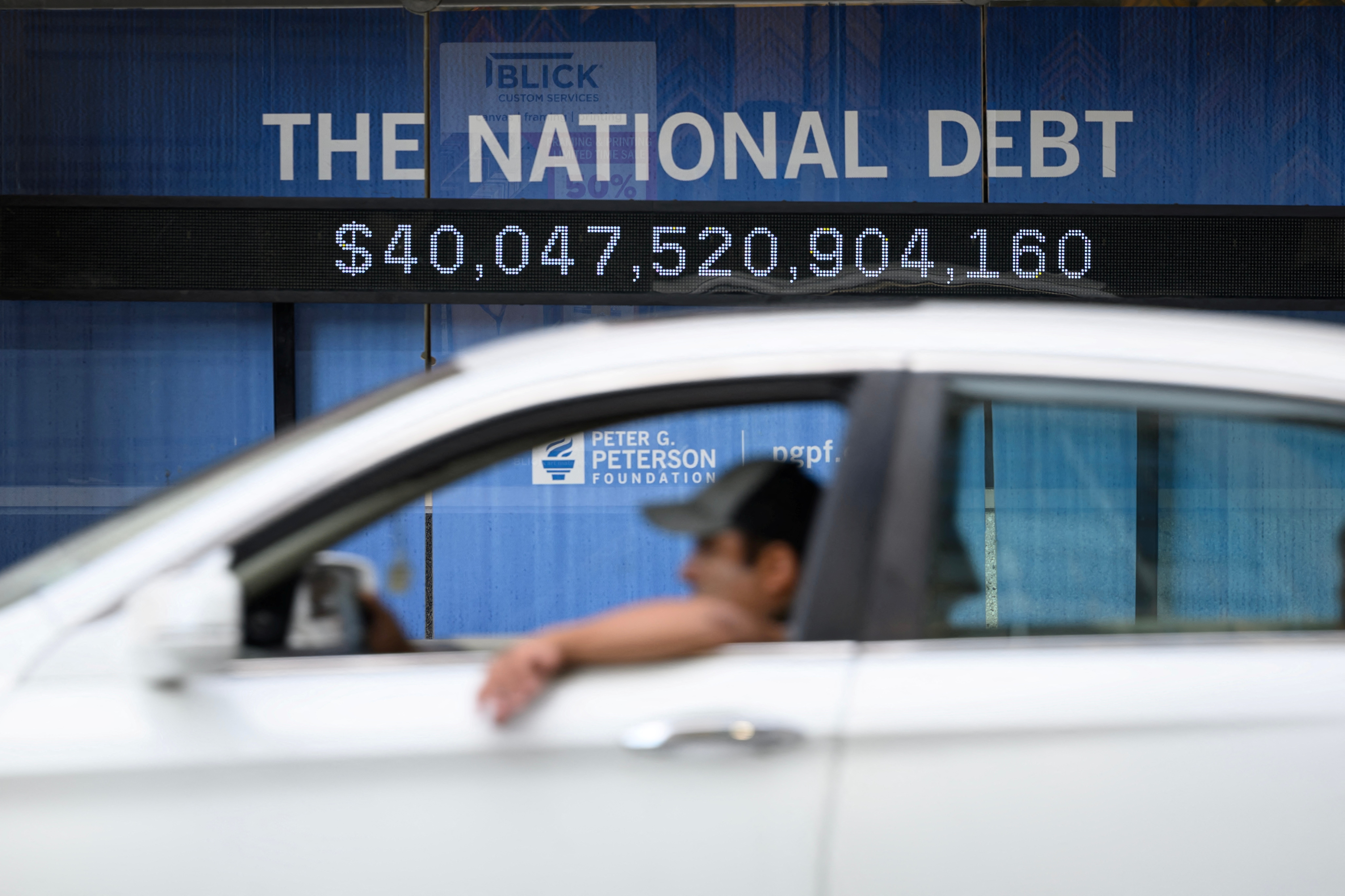 A car parked in front of a national debt counter showing more than $40 trillion.