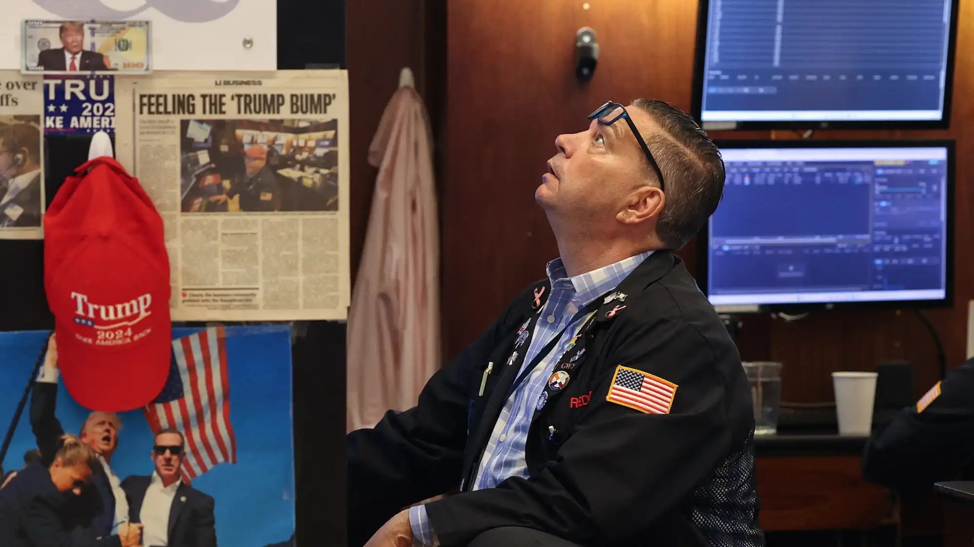 A stock trader looks at a screen next to a cork board covered in images of Trump.