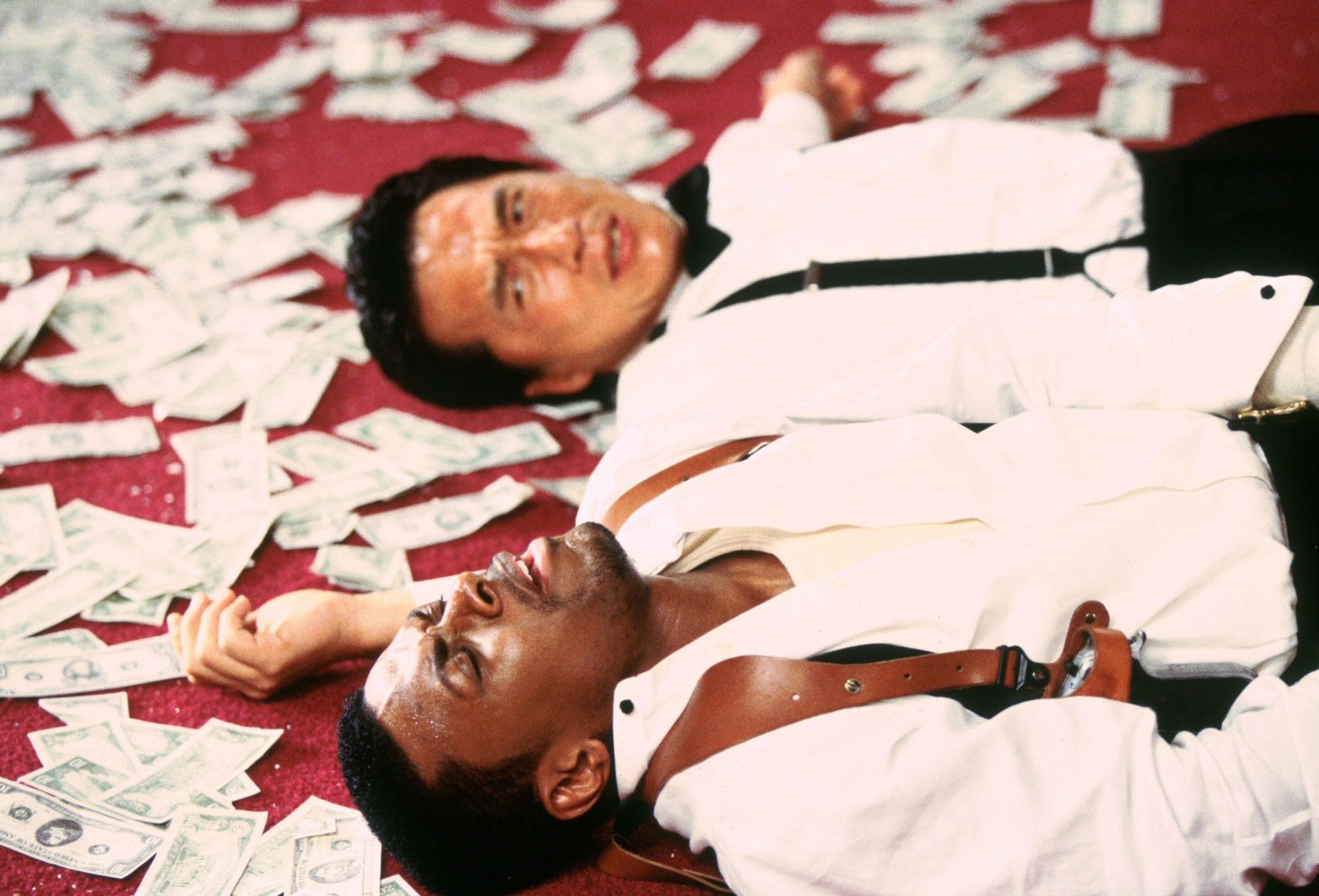 Chris Tucker and Jackie Chan lay on a bunch of money in a still from the 1998 film 