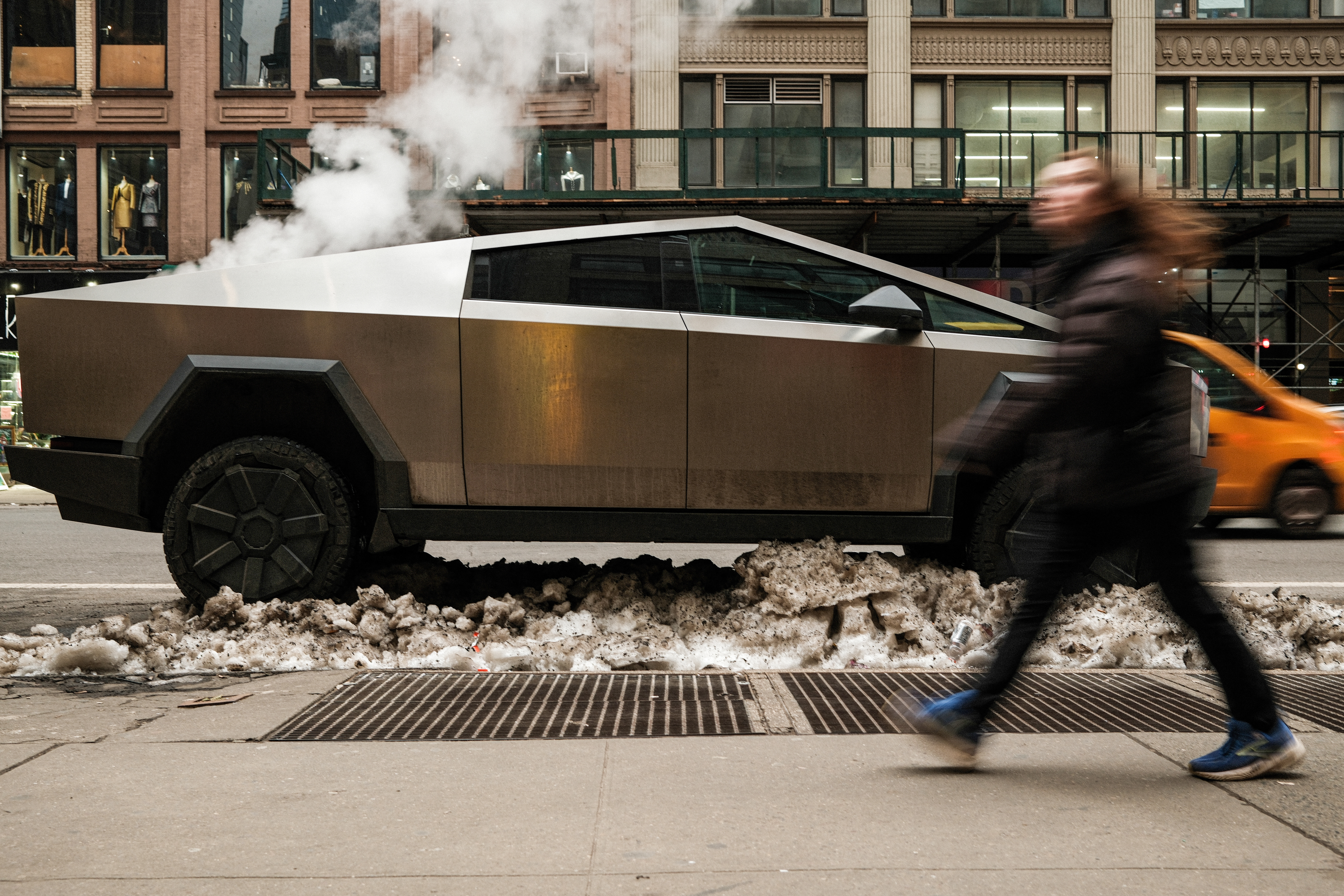 A woman walks by a cybertruck parked on the street.