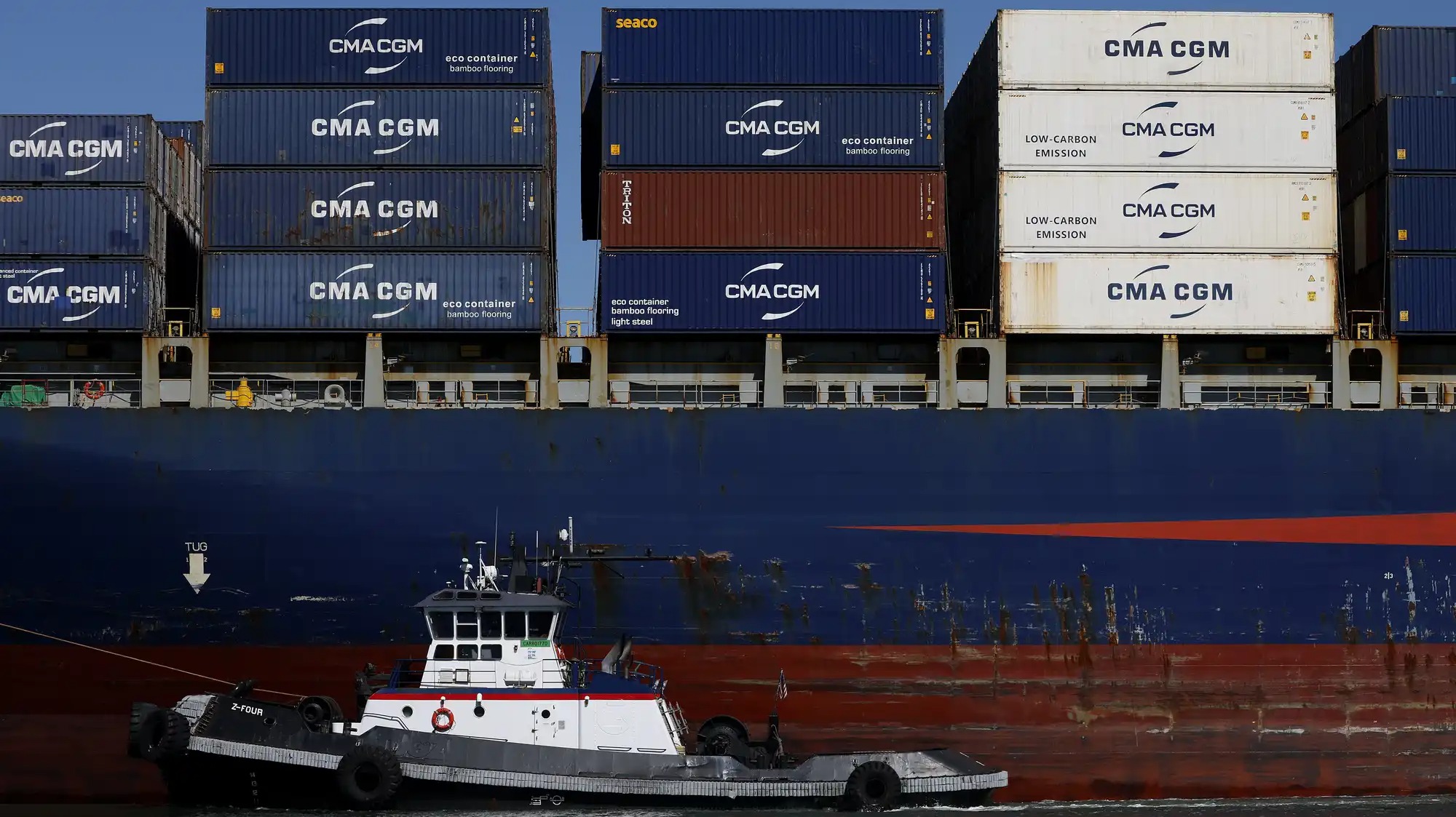 Shipping containers on a freighter with a tugboat on the foreground.