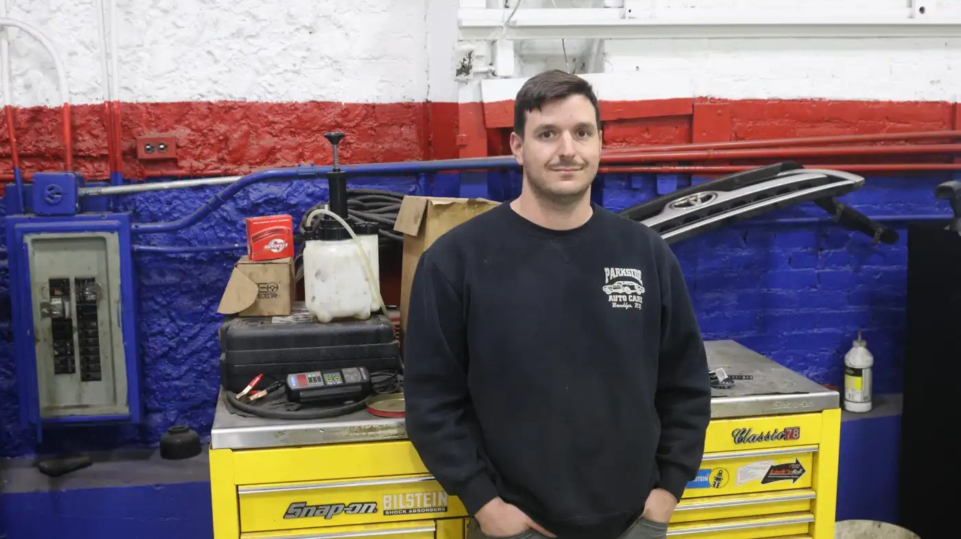 A man poses for a portrait in an auto garage.