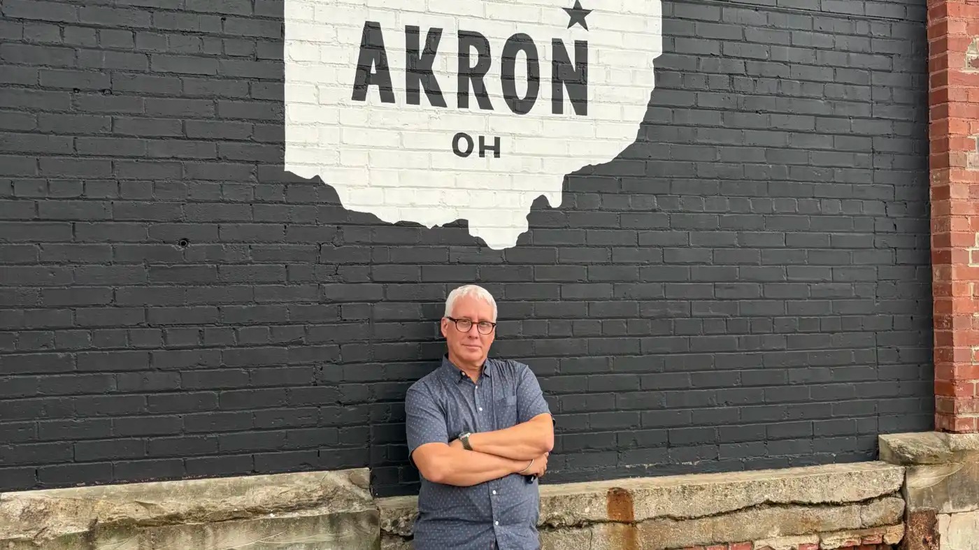 David Brancaccio stands in front of a mural for Akron, Ohio.