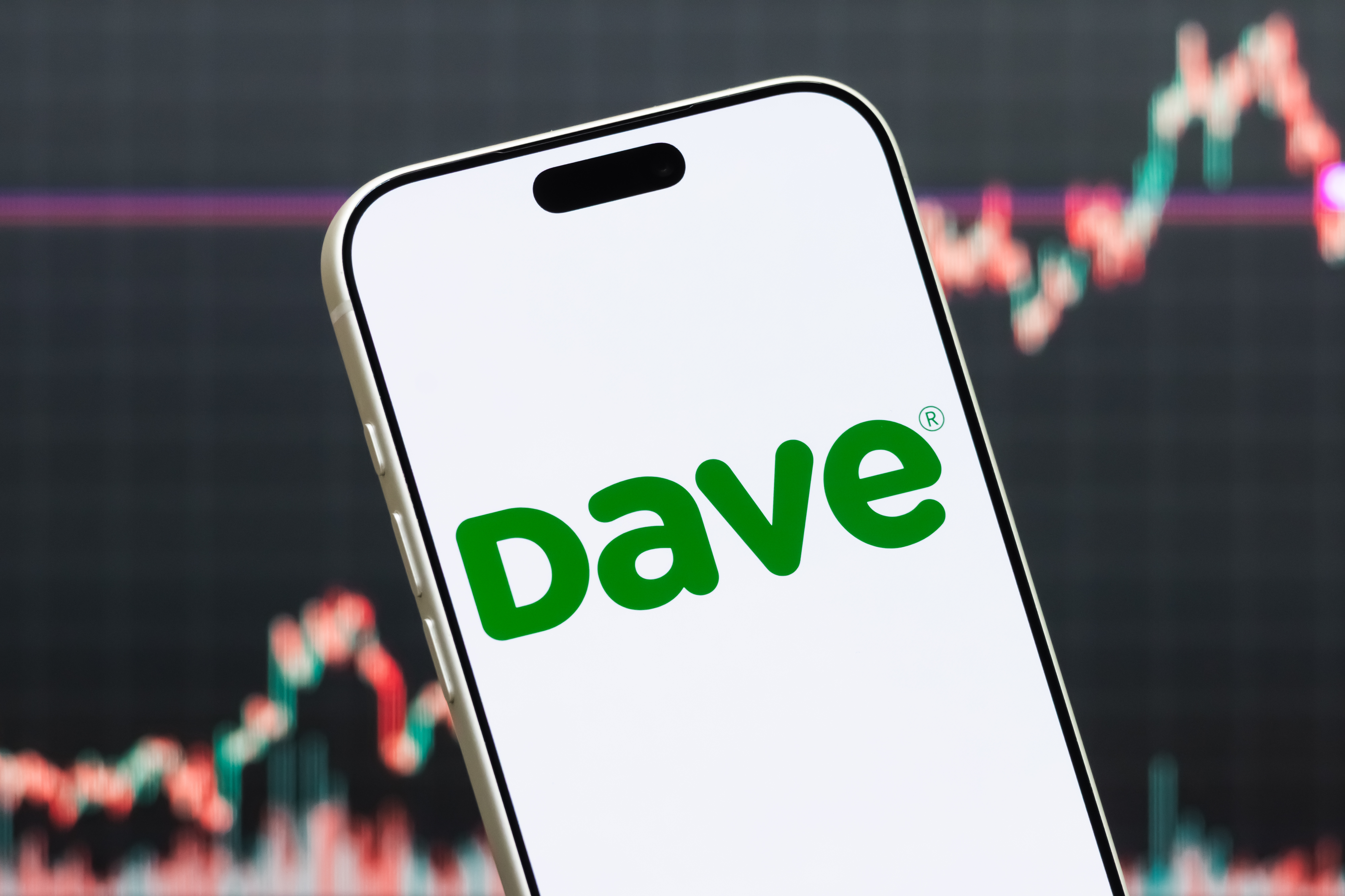 Dave app phone screen in front of stocks