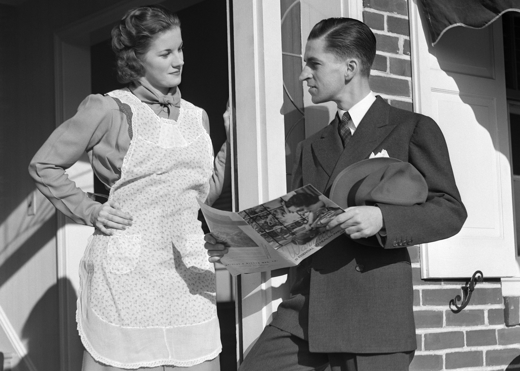A salesman talks to a homeowner at her front door. He shows her a catalog. 