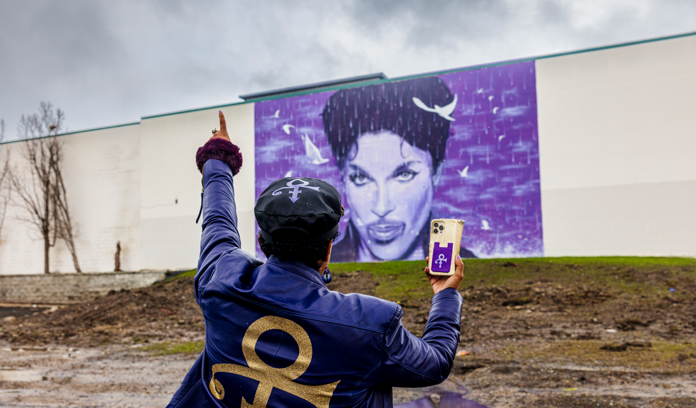  a visitor poses in front of a mural of Prince on a wall 