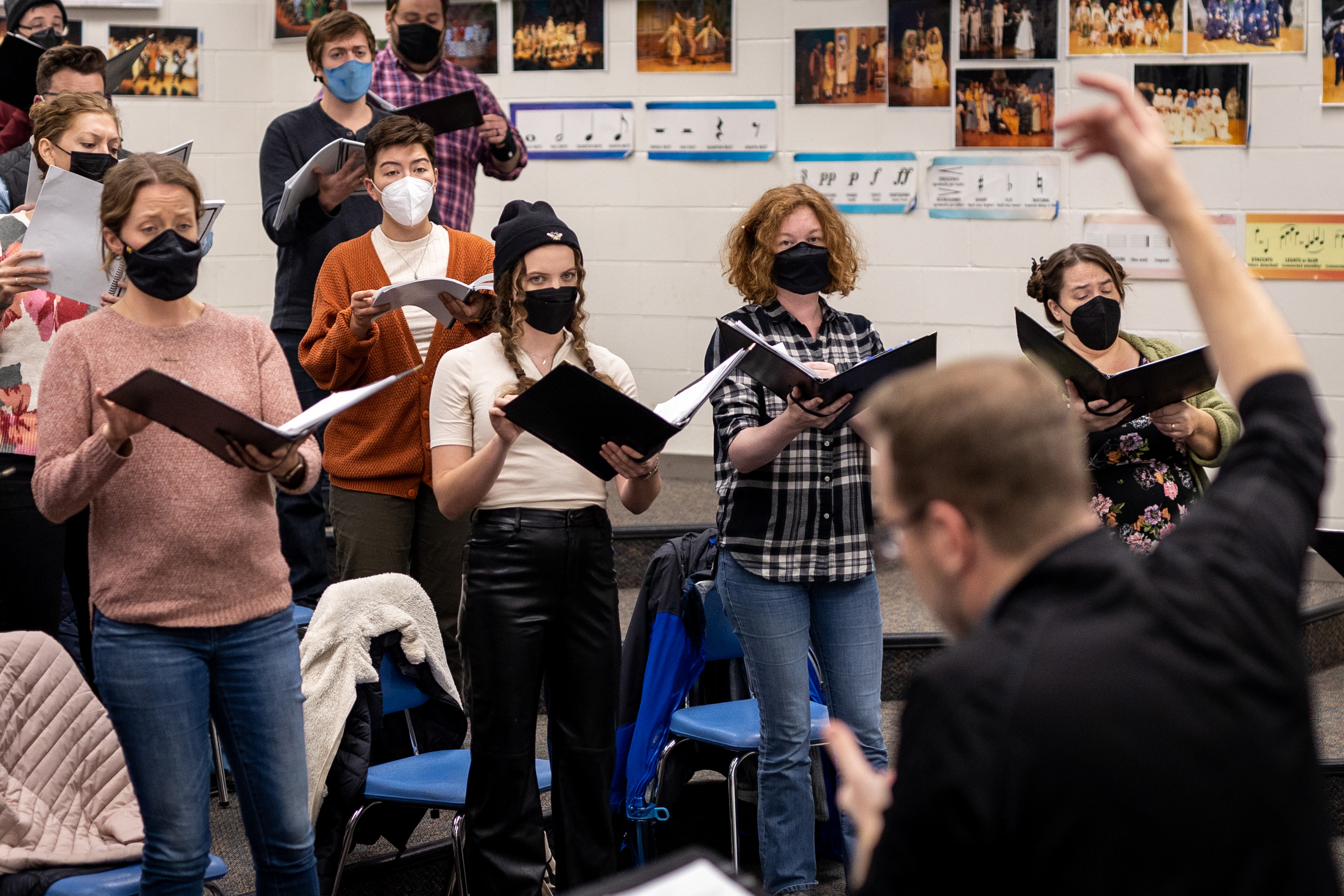 Masked choir members hold music binders during a rehearsal.